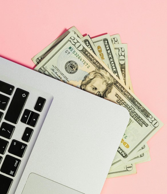 Image of several 20 dollar bills under a laptop keyboard